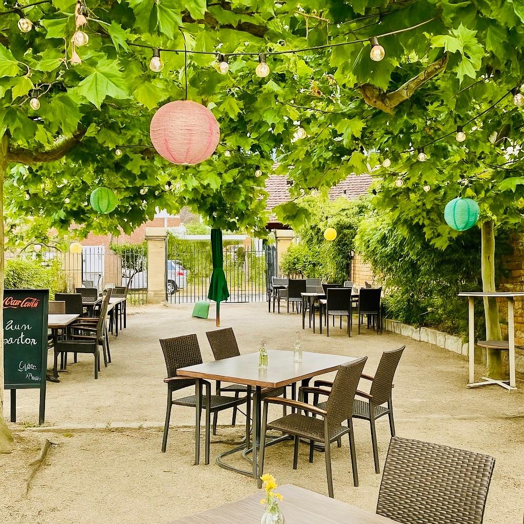 Der Biergarten unter Platanen mit Lichterketten und bunten Lampions
